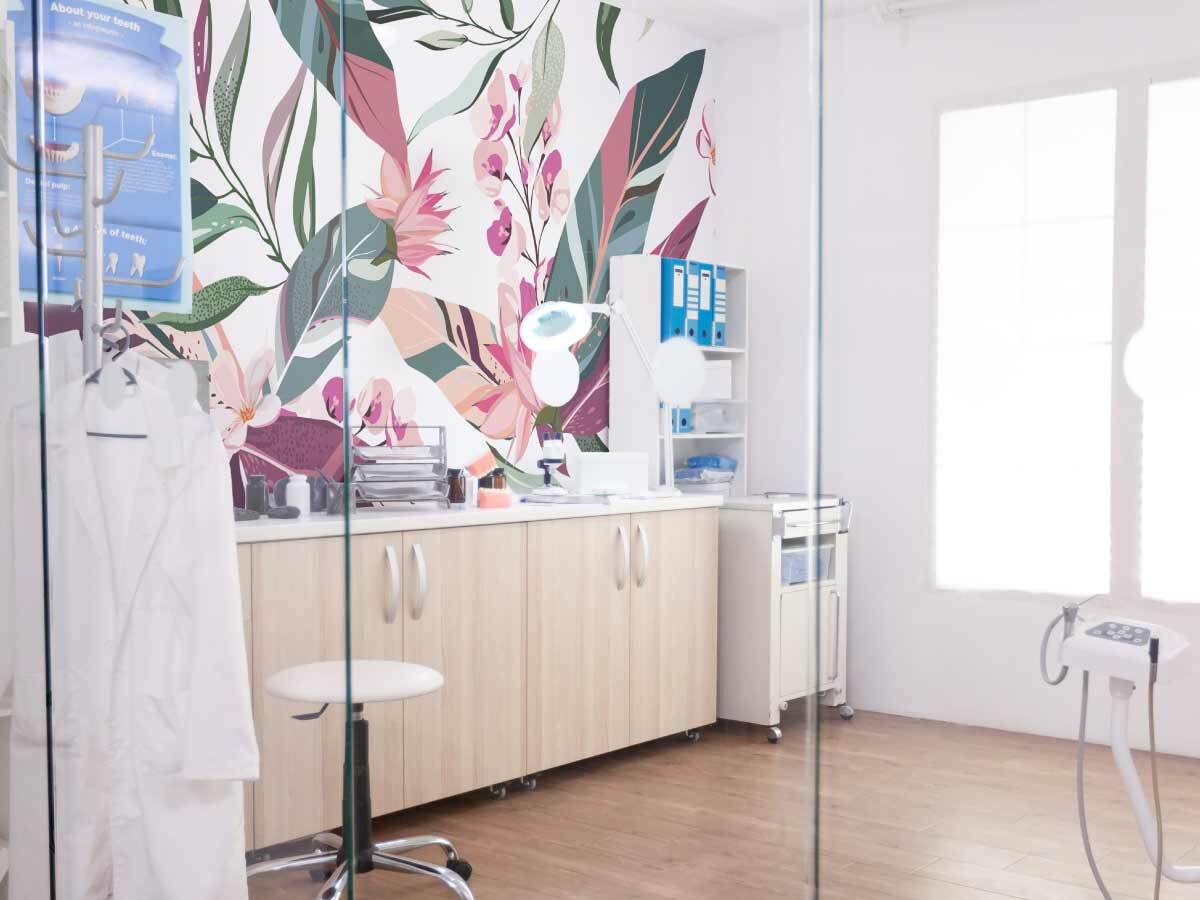Cabinet médical avec un papier peint aux motifs de feuilles roses sur fond blanc, créant une ambiance lumineuse et apaisante.